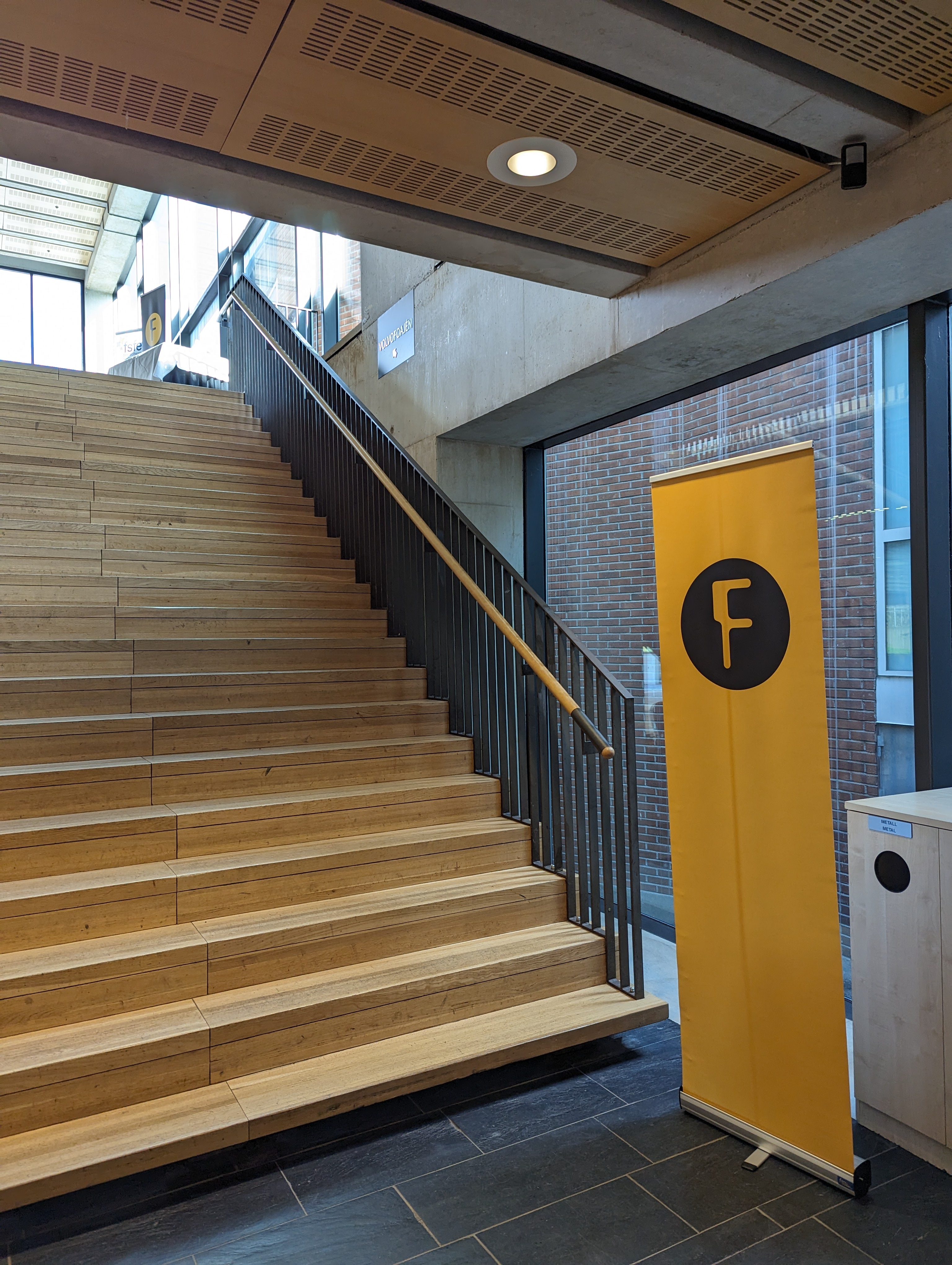 Picture showing the venue with stairs going up to the main hall and a sign with the foss-north logo.