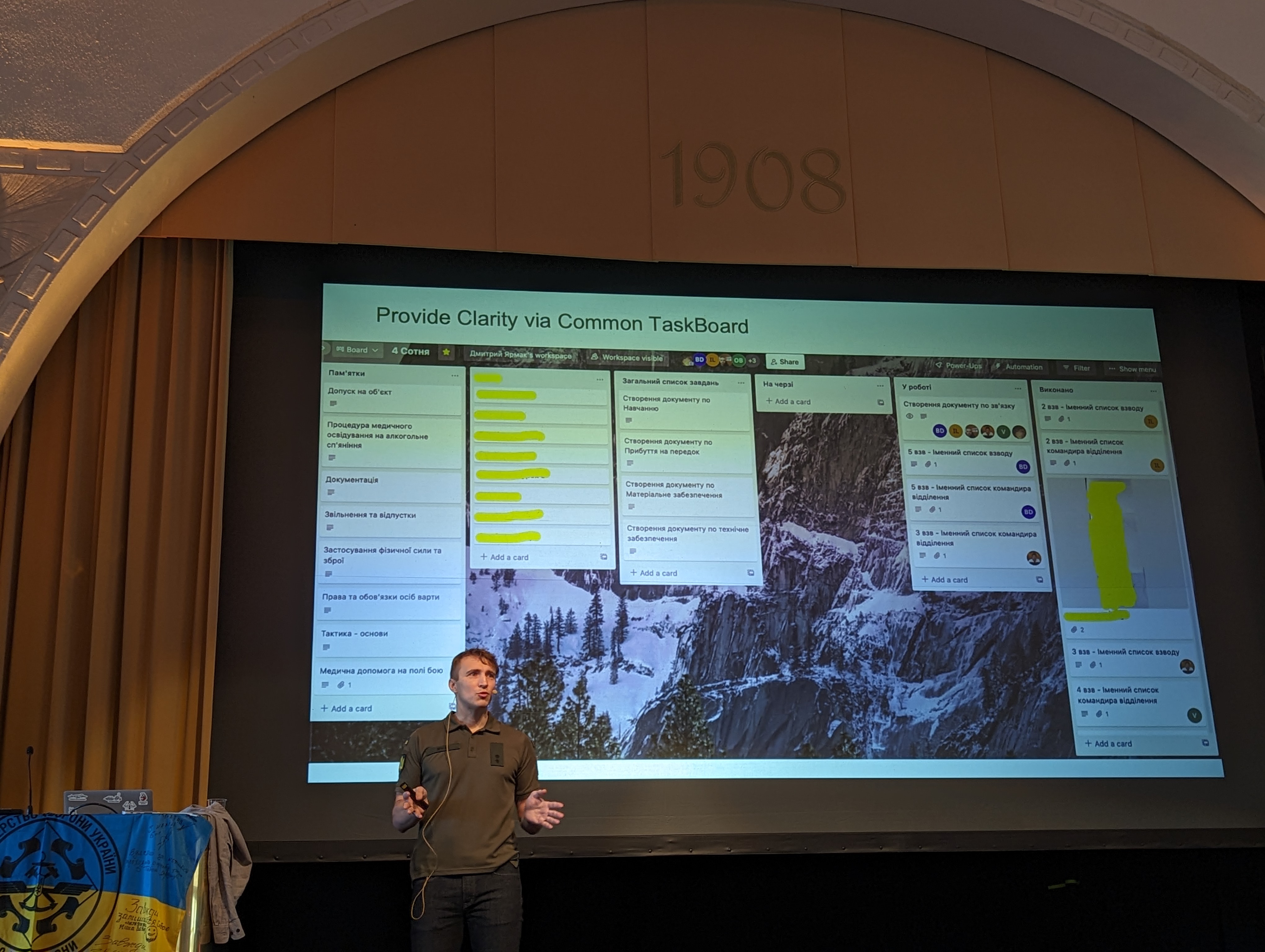 Dmytro Yarmak standing on stage while his slide show a screenshot
of a kanban board in Trello.